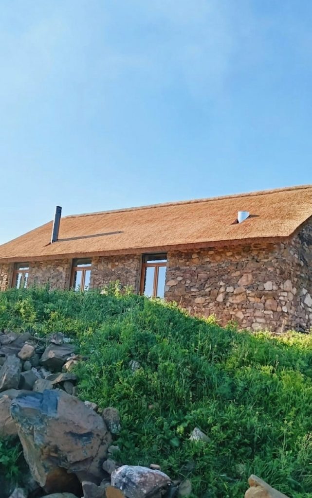 Exterior view of Beta-0 architectural firm's mountain lodge design combining traditional stonework and authentic thatched roofing in Ciudad Real province