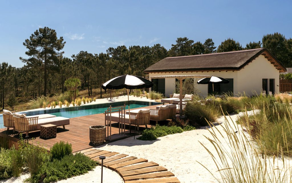Timber decked pool terrace with teak lounge furniture and black parasols at Villa Stark, Comporta, Portugal