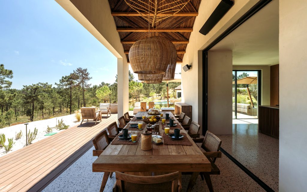 Covered outdoor dining terrace with reed lath ceiling, rattan pendant lamps, and timber dining table at Villa Stark, Comporta